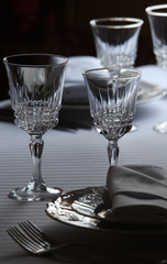 Served cutlery sets, plates, napkins, empty crystal wine glasses, on tables in a restaurant.