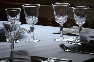 Served cutlery sets, plates, napkins, empty crystal wine glasses, on tables in a restaurant.