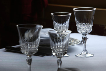 Served cutlery sets, plates, napkins, empty crystal wine glasses, on tables in a restaurant.