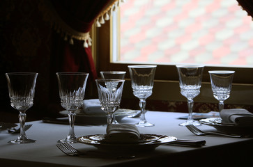 Served cutlery sets, plates, napkins, empty crystal wine glasses, on tables in a restaurant.