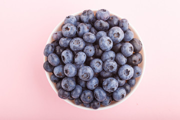 Fresh blueberry in white bowl on  pink background. top view.