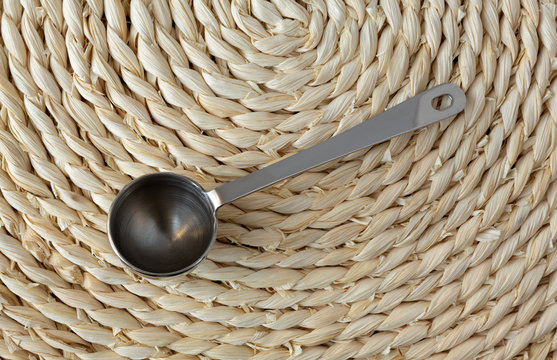 Metal coffee measuring scoop on a woven straw background.