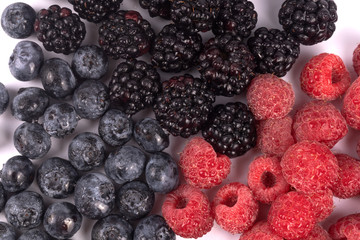 Close-up photo of wet set of blackberries, blueberries and raspberries laying on white background