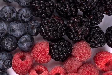 Photo of mixed wet blackberries, blueberries and raspberries laying on white background