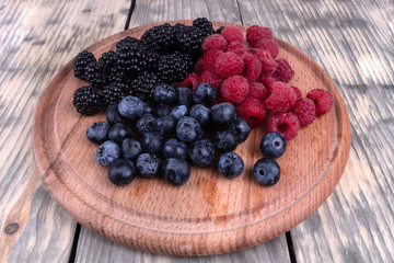Composition of three types of summer berries laying on textured wooden plate