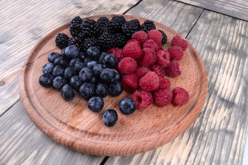 A set of blackberries, blueberries and raspberries laying on a wooden plate