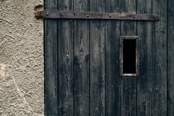 Spooky dark vertical window in rustic ancient textured wood door with rusty metal hinge / Halloween horror concept