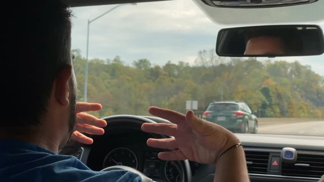 A male millennial driver experiences road rage behind the wheel on the interstate. Rudely gestures to passing vehicle showing the middle finger. Shot at 48fps.  	