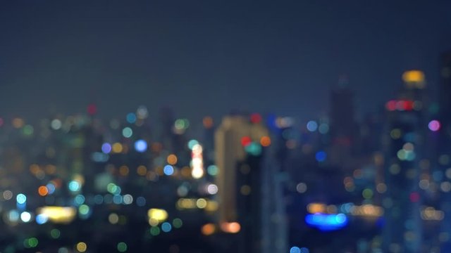 Bokeh background of skyscraper buildings in downtown city with lights, Blurry photo at night time.  illuminated Cityscape