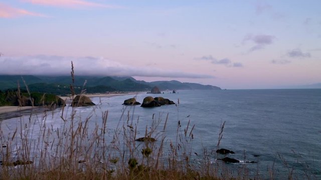 Static wide shot overlooking rocky Pacific ocean shore from a grassy hill in fall sunset colors