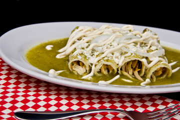 Delicious Mexican enchiladas bathed in tangy green chile sauce, layered with creamy cheese and a dollop of sour cream, perfect for authentic cuisine lovers.