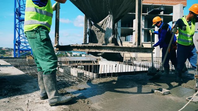 Workers pour concrete onto a floor, leveling it.