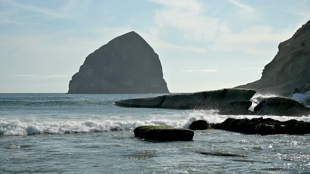 Static shot featuring Pacific ocean wave with the view over Haystack rock at Cape Kiwanda beach