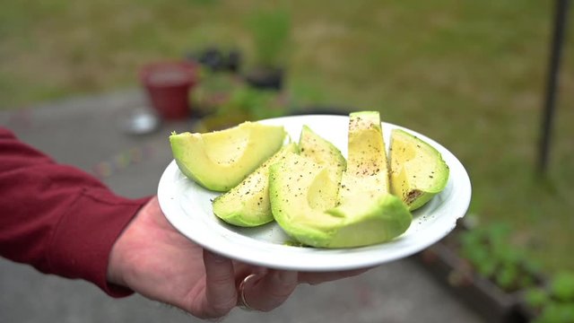 Rotating close up of a senior mand hand holding a plate with peeled and sliced seasoned avocados