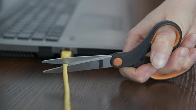 Cut a cord. Disconnect internet concept. Scissors cut the cable included in the laptop.