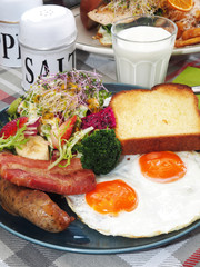 English breakfast with fried eggs, bacon, sausages, toasts and salad on the plate 