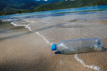 A plastic bottle washed away by the waves on the edge of an empty tropical beach.