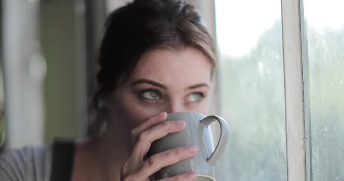 Young adult female having morning coffee looking out of window