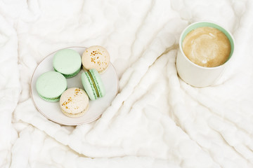 Top view with cozy atmosphere, fragrant cappuccino and sweets for breakfast. Cup of coffee and macaroons on white fluffy background with copy space for text. Top view, flat lay.
