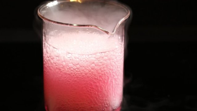 Pink chemical substance that boils in a becker isolated on a black background