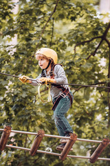 Cute child in climbing safety equipment in a tree house or in a rope park climbs the rope. Hike and kids concept. Toddler age