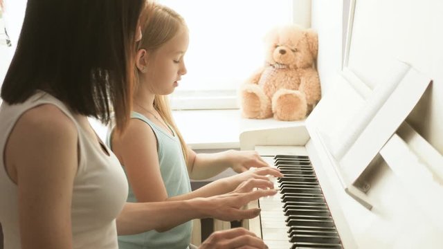 Mother teaching daughter to play piano at home.