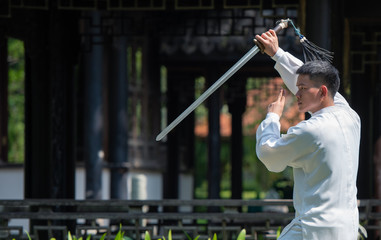 Asian man working out with Tai Chi sword in the morning at the park, Chinese martial arts, healthy...