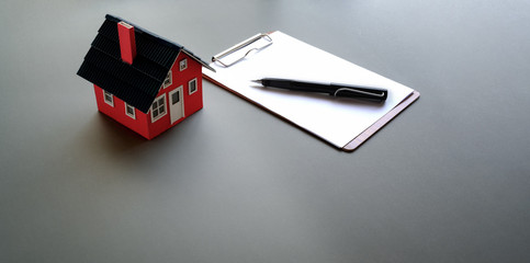 Small house model with note paper and pen in grey background