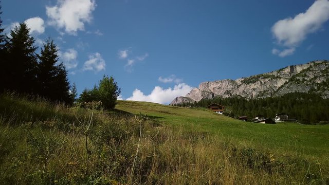 Clouds speeding across the sky, forming and desolving, swirling over a green meadow in the Italian Alps.