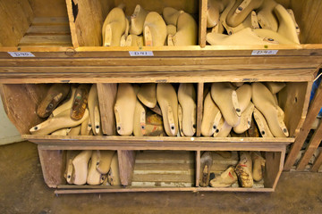 Old wooden shoe lasts in a wooden bin are separated by varioud sizes.