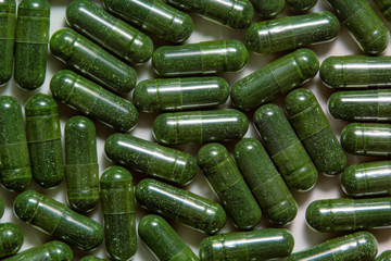 Green chlorella powder capsules background. Natural supplement pills, alternative medicine