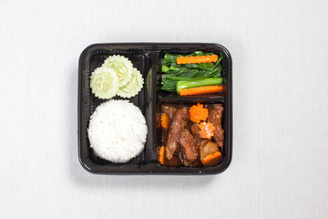 Baked pork rice put in a black plastic box, put on a white tablecloth, food box, Thai food.