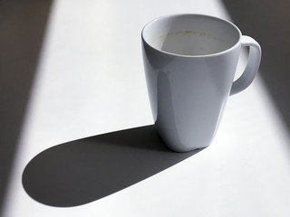 Empty dirty white mug casting a long shadow on a white table
