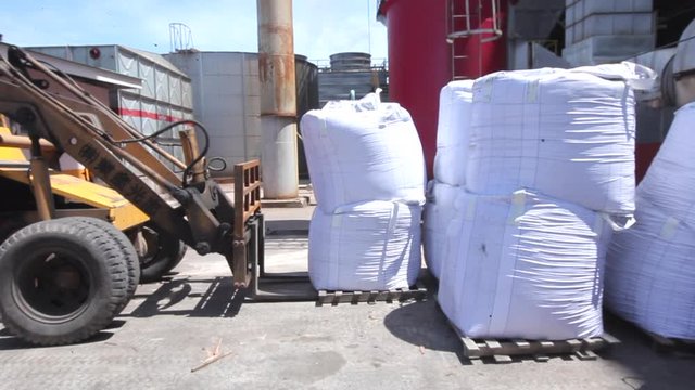 Side shot of a tractor backhoe forklift handled by a worker move in and carry up a heavy bale of mass inside the factory area (Kilang Kelapa Sawit)