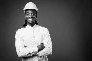 Young handsome African businessman with hardhat against brown background