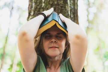 Young woman holding a book on her head outdoors