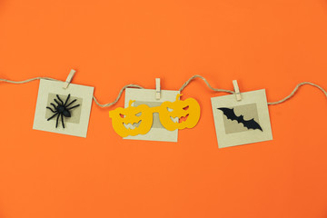 Table top view aerial image of decorations Happy Halloween day background holiday concept.Flat lay objects to party pumpkins photo prop and spider & bat hang on paper clips on orange wallpaper.