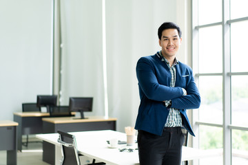 Portrait of smart and handsome Asian businessman standing in the office close up.  Modern work place and young businessman concept.