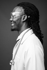 Young handsome African man doctor wearing protective glasses against brown background