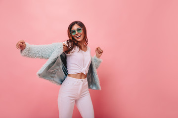 Lovely slim girl posing with sincere smile. Pretty long-haired female model dancing with hands up on pink background.