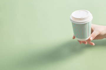 disposable paper cup with coffee in women hand on green background