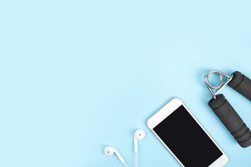 Top view. Sports accessories with dumbbells, smartphones, headphones in a blue background. With copy space.