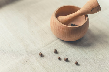 rustic flat lay, wooden mortar with wooden pestle for grinding spices on linen background and with peppercorns on windowsill