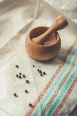 rustic flat lay, wooden mortar with wooden pestle for grinding spices on linen background and with peppercorns on windowsill