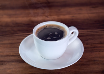 Cup of aromatic coffee, close up view. White coffee cup and saucer on brown wooden table. Texture of wooden desk. Selective soft focus. Blurred background