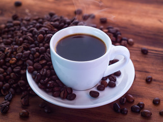 Composition of coffee beans pilled on brown table and saucer with cup full of espresso. Texture of...