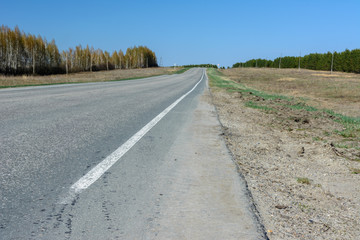 A winding highway stretching into the distance against the backdrop of a beautiful spring landscape, fields, meadows, forests and hills. Road stripes on asphalt.