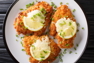 Serving romano chicken cutlet fried breaded with lemon and green onion closeup on a plate. Horizontal top view