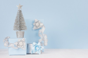 Elegance soft christmas home decoration - silver small fir with blue gift boxes with shiny ribbons and snowflakes on light white wood board and pastel blue wall.