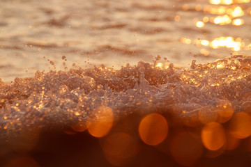 A rushing wave splashes against the sea shore in golden sunlight